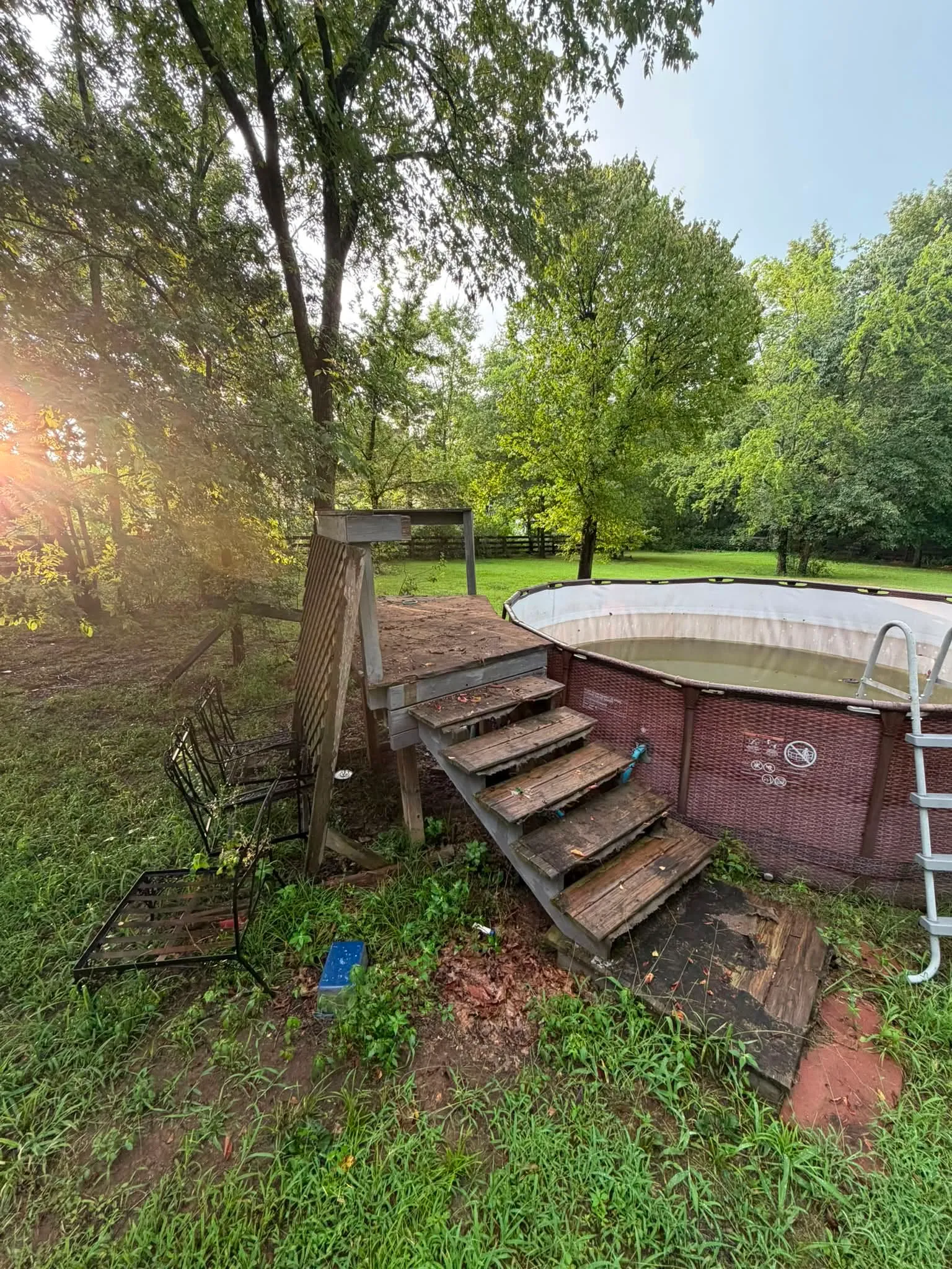 An above-ground pool with its wooden steps in a wooded back yard, before the tear-out
