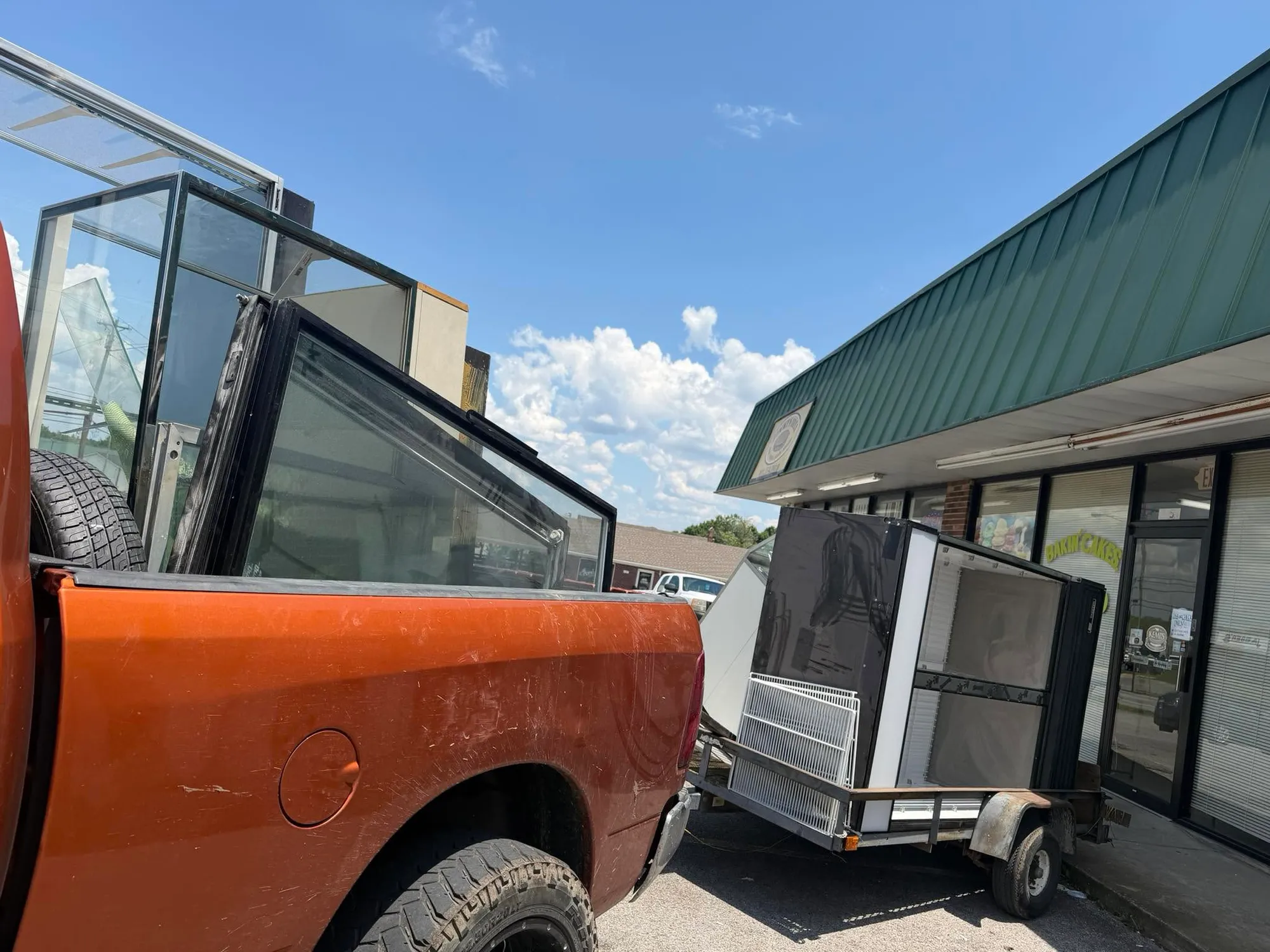 A glass bakery display case and equipment loaded on a trailer outside a closed storefront