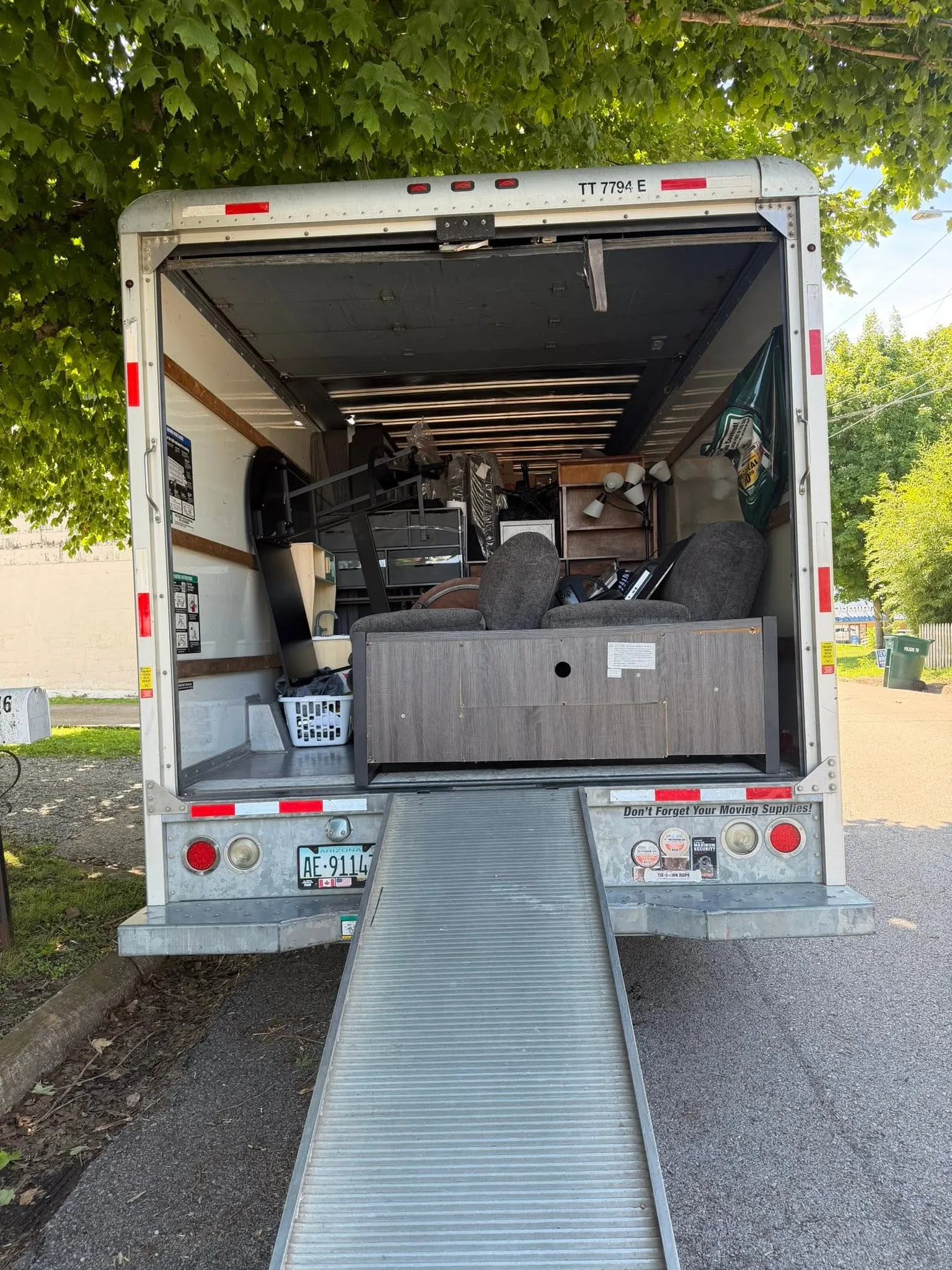 The box truck backed into a driveway with its ramp down, loaded with furniture