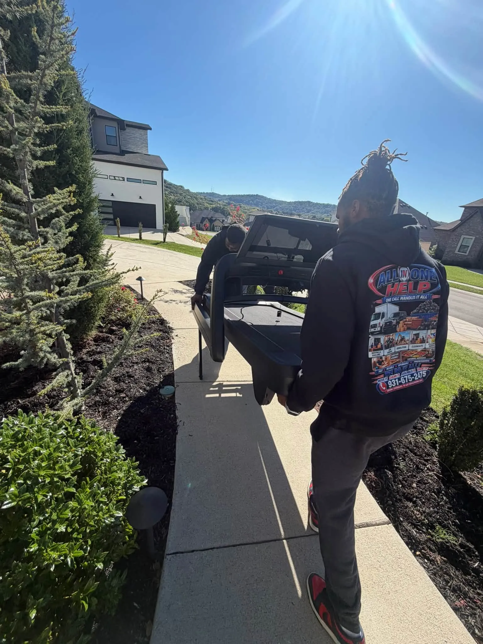 A crew member carrying a flat-screen TV up a sidewalk beside a new house