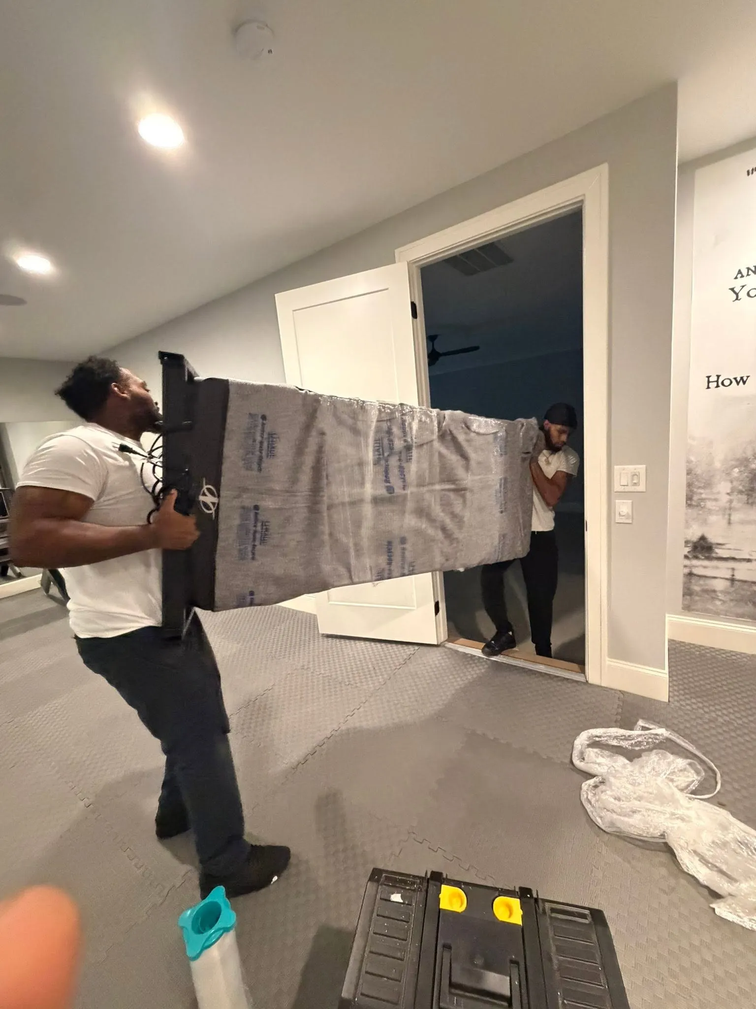 A crew member carrying the deck of a treadmill through a house