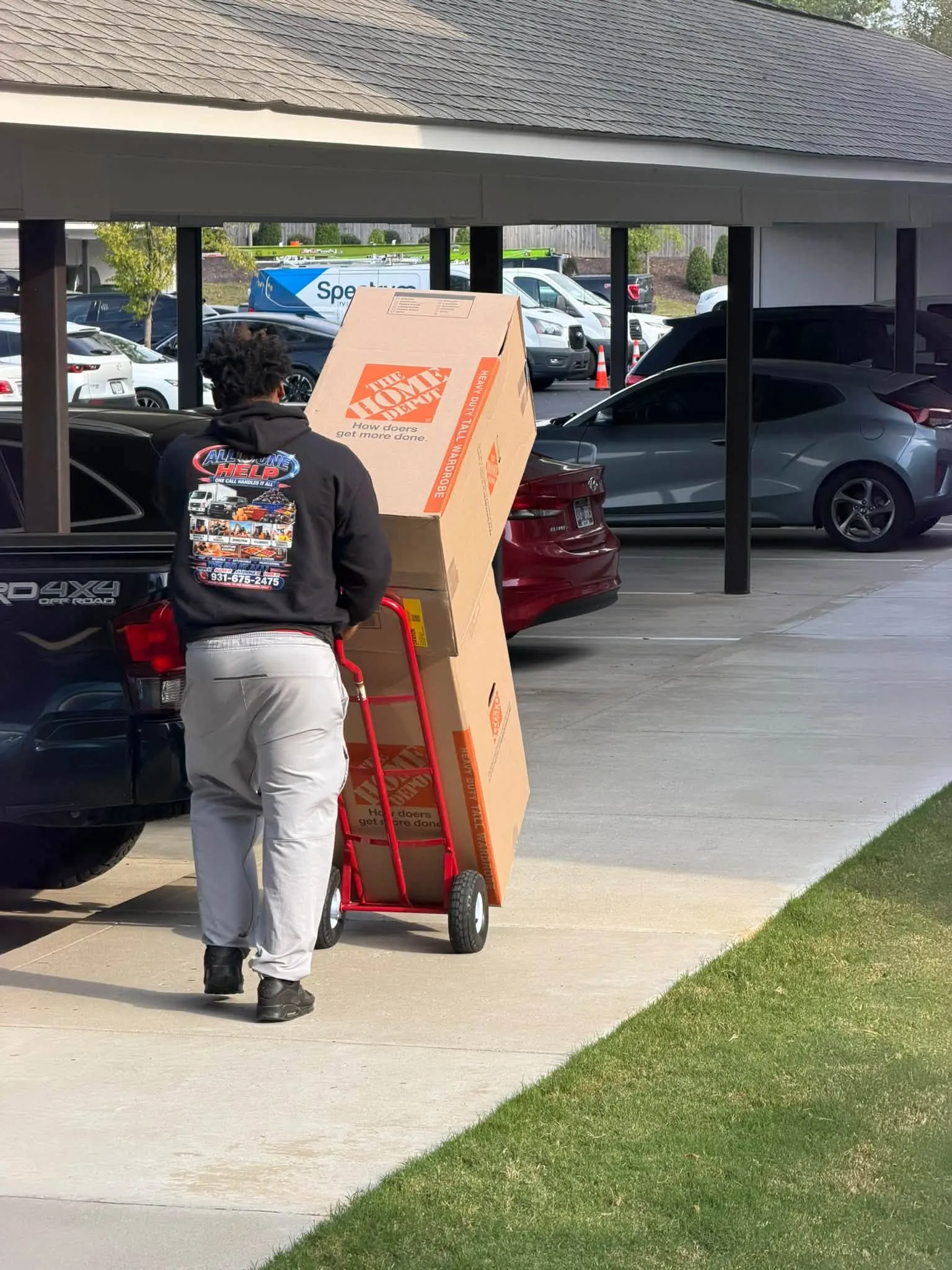 A crew member wheeling a hand truck stacked with boxes past a row of carports