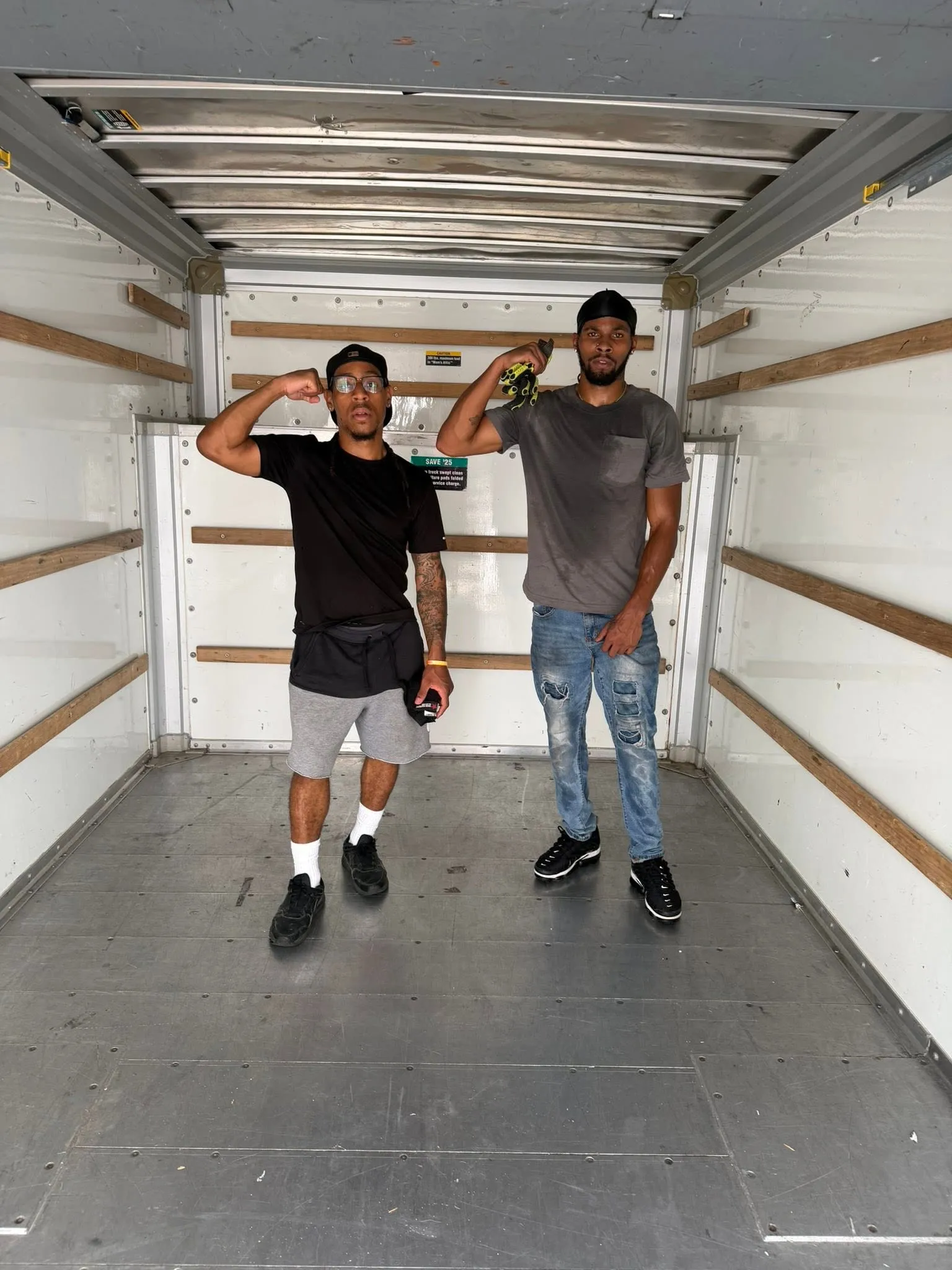 Two men from the crew standing in the empty box truck, saluting the camera