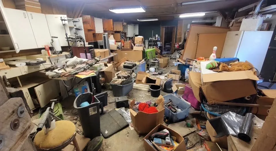 A basement workshop with boxes, bags, furniture and tools covering the whole floor