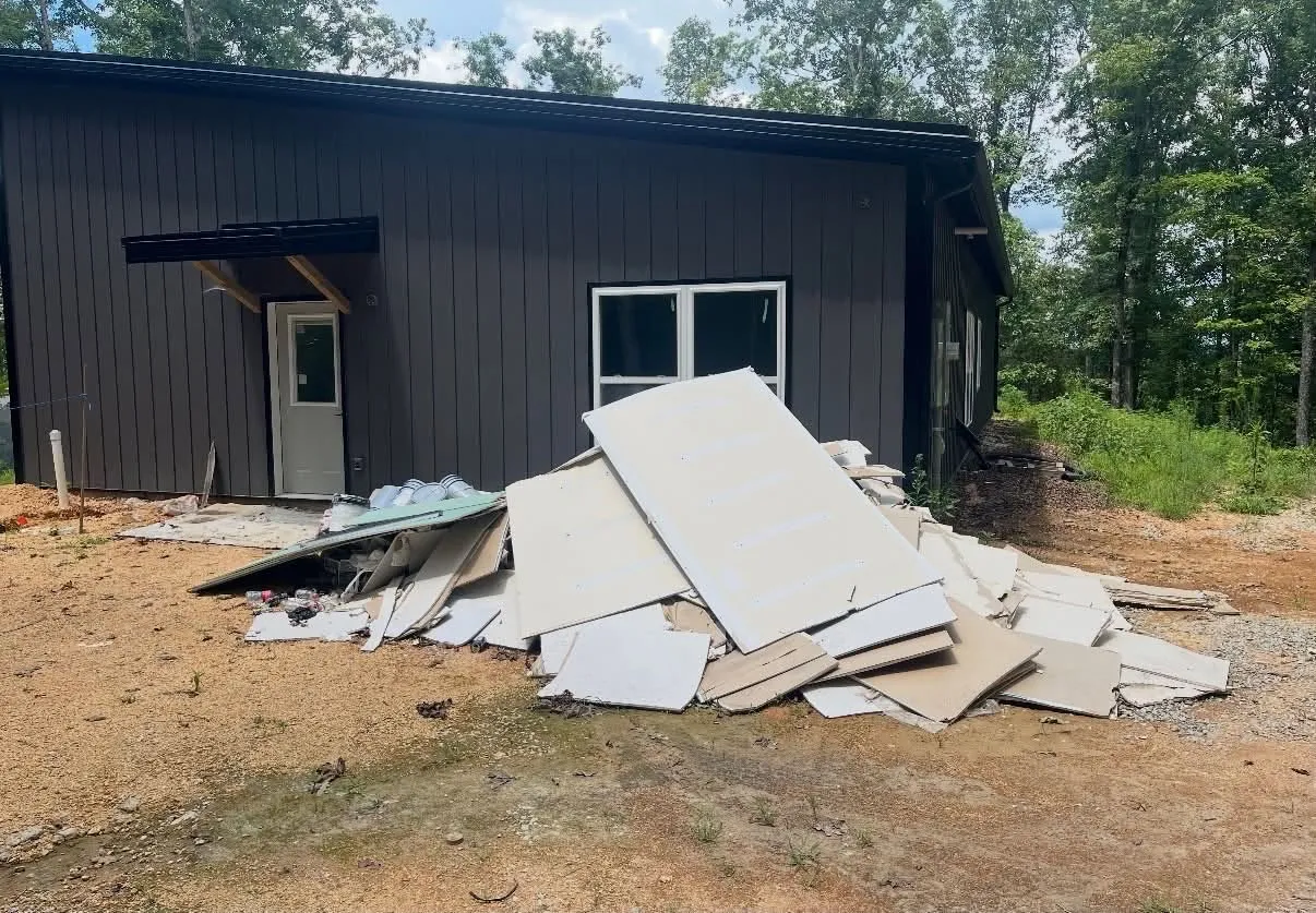 A pile of torn-out drywall sheets on the dirt beside a dark metal building