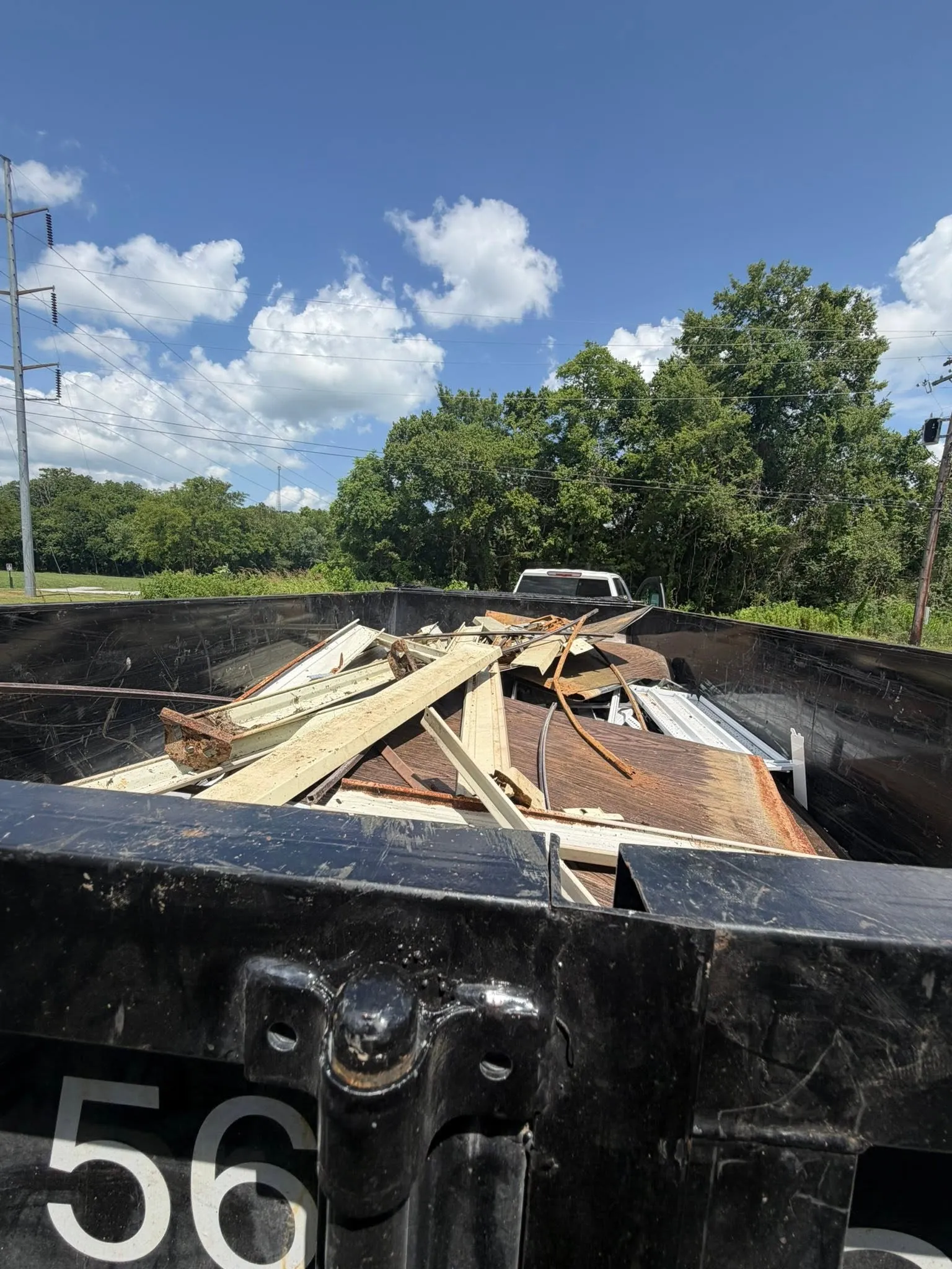 A roll-off container numbered 56 filled with torn-out boards and debris under a blue sky
