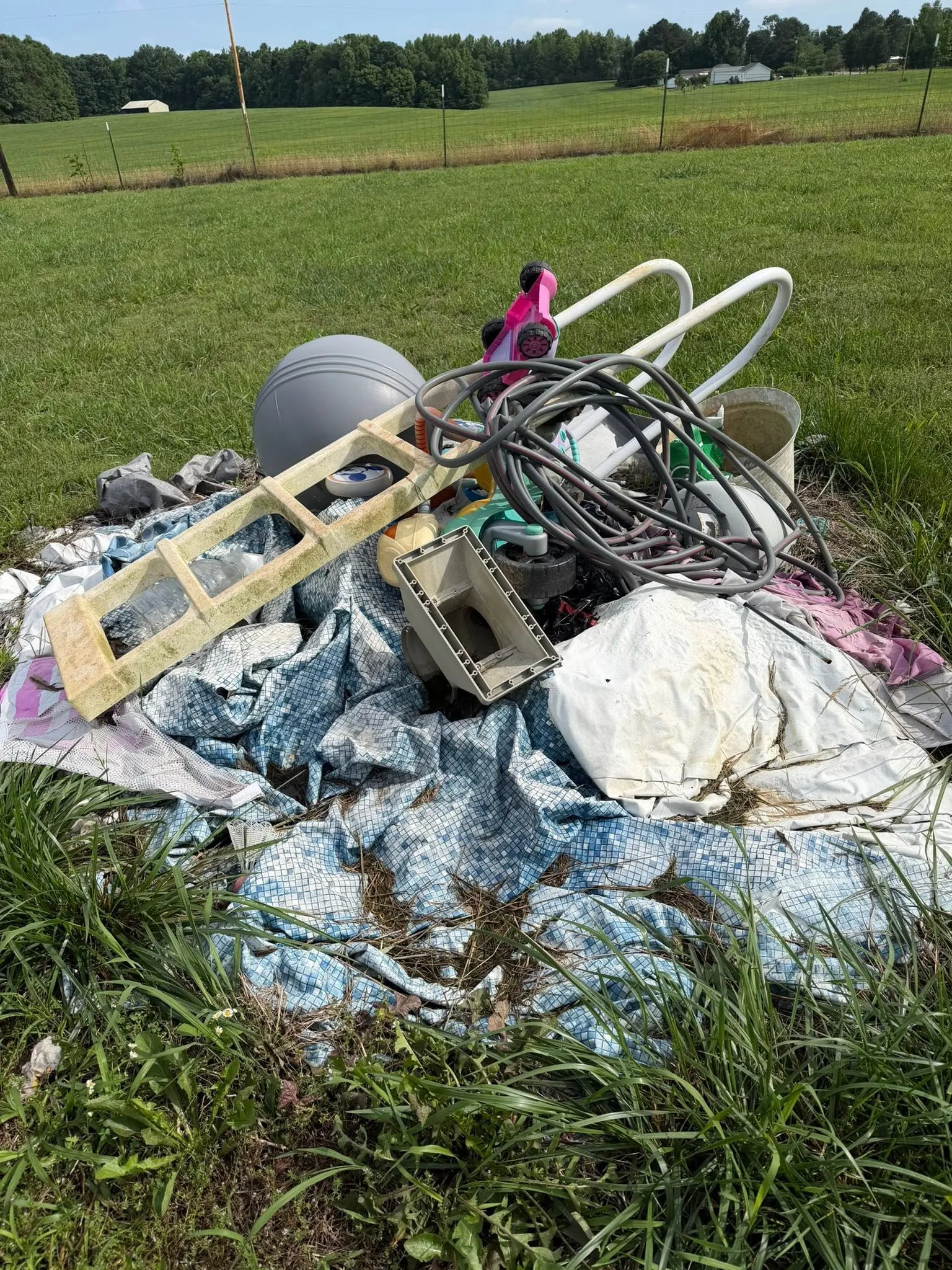 A heap of chairs, shelving, tarps and metal in a mowed field, waiting to be loaded