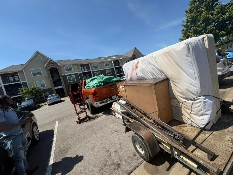 A mattress, a dresser and boxes loaded on the trailer behind the orange pickup at an apartment complex