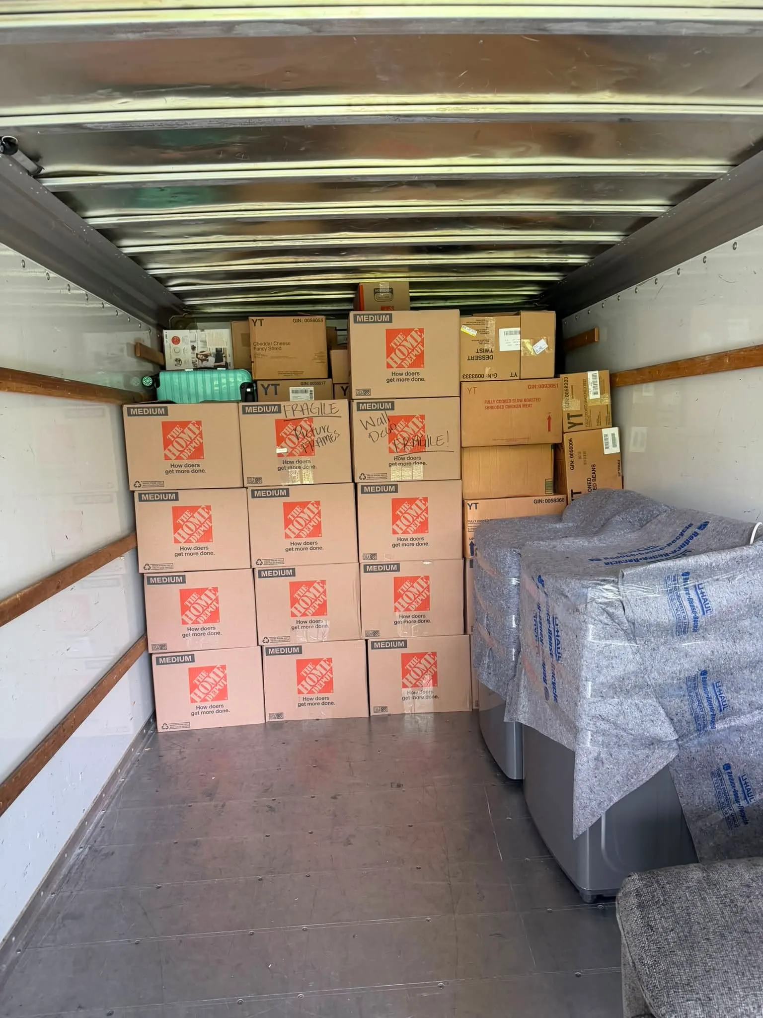 Moving boxes stacked neatly inside the box truck beside a wrapped mattress