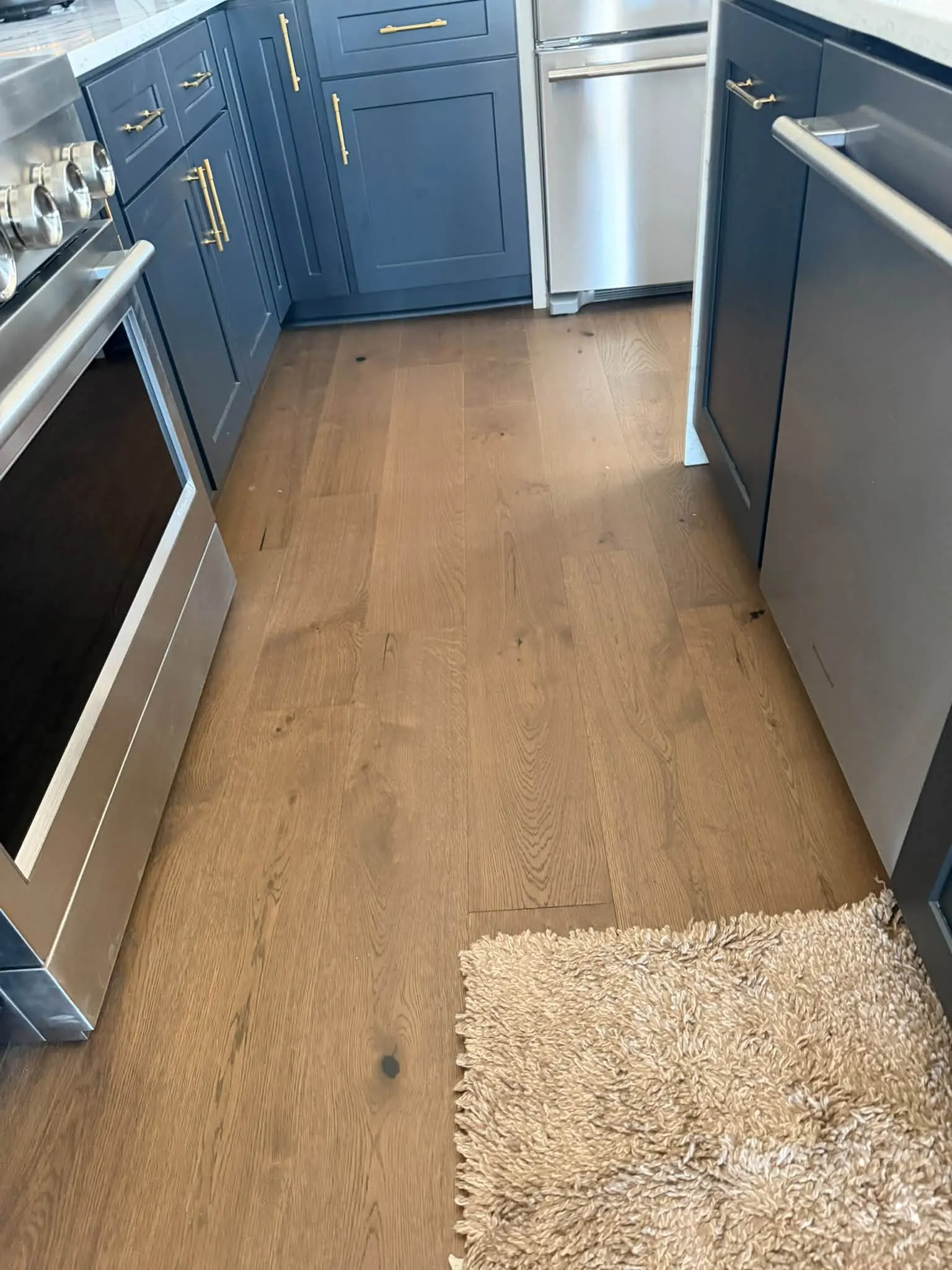 A new kitchen with blue cabinets and a clean hardwood floor after the post-construction clean