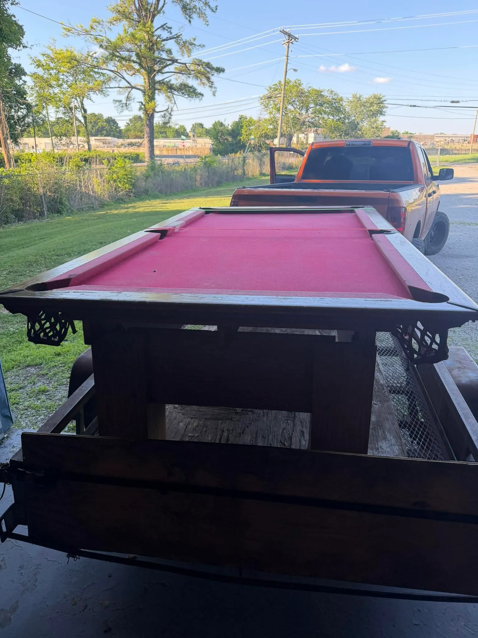 A pool table with red felt strapped on the trailer behind the pickup