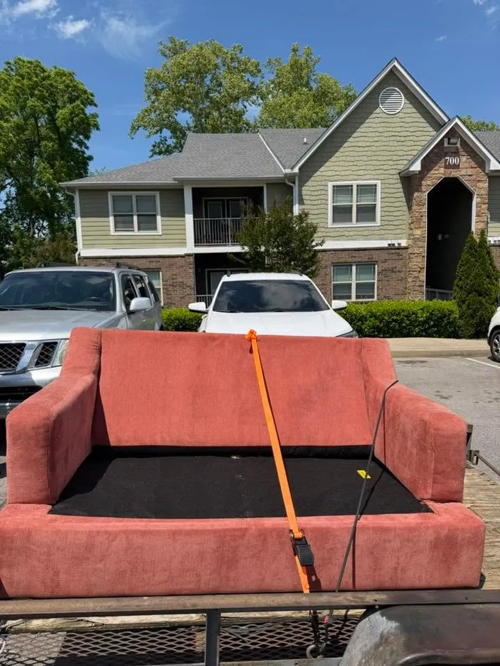 A red couch strapped down on the trailer in an apartment parking lot