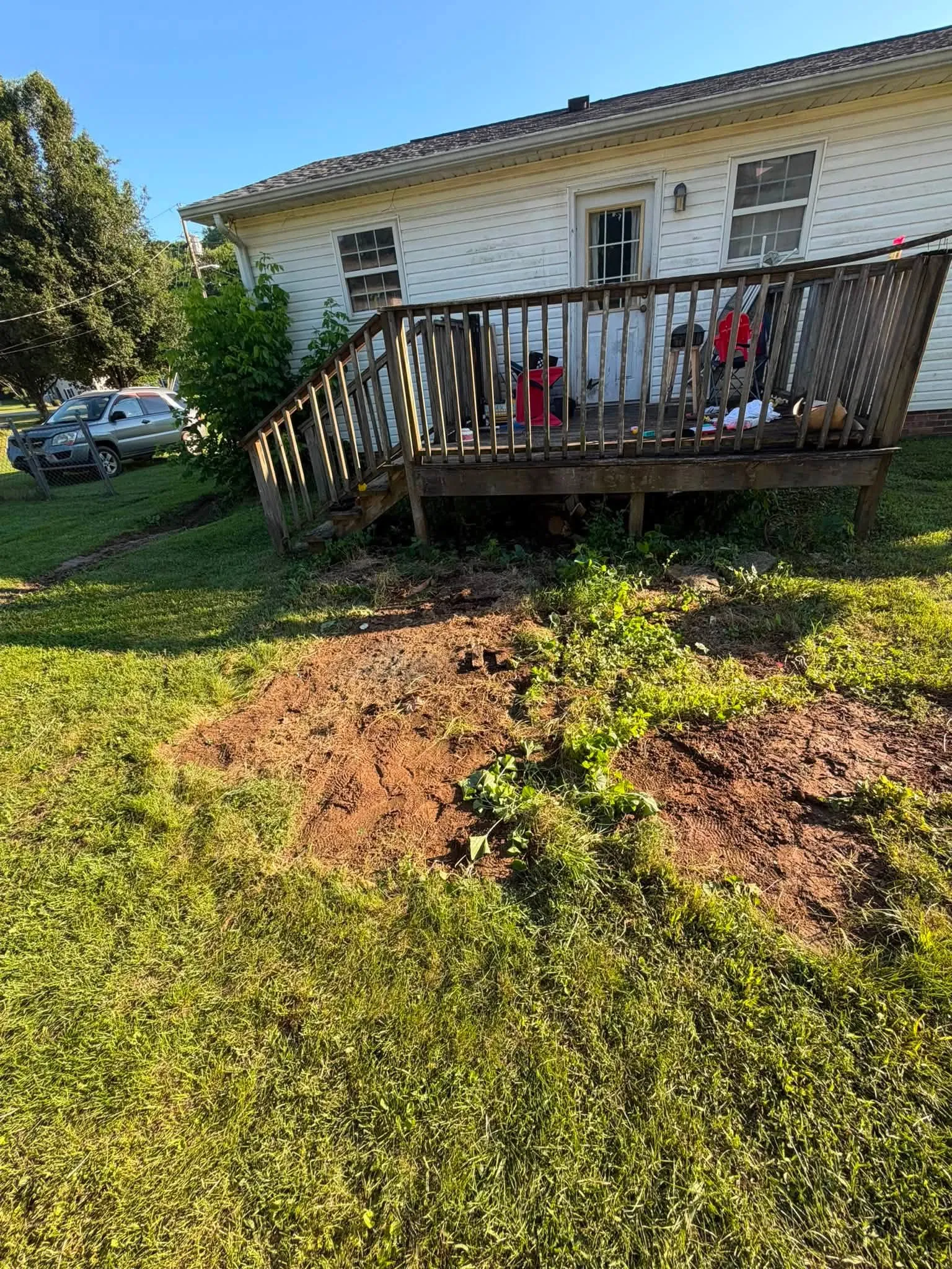 The same side yard with the junk gone, bare dirt where the pile sat, the deck behind
