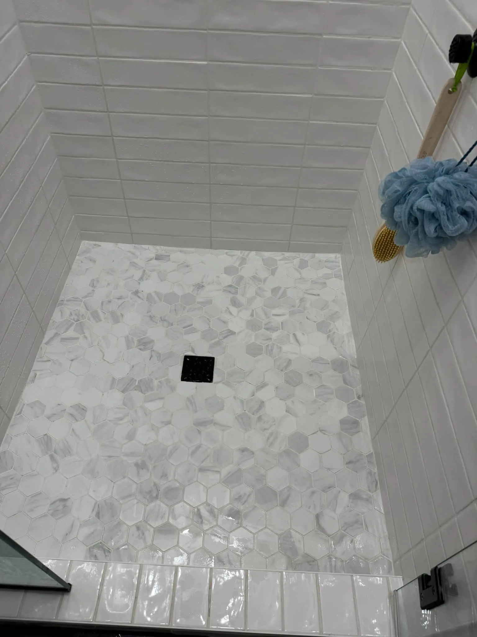 A white tiled shower with a hexagon floor, scrubbed clean